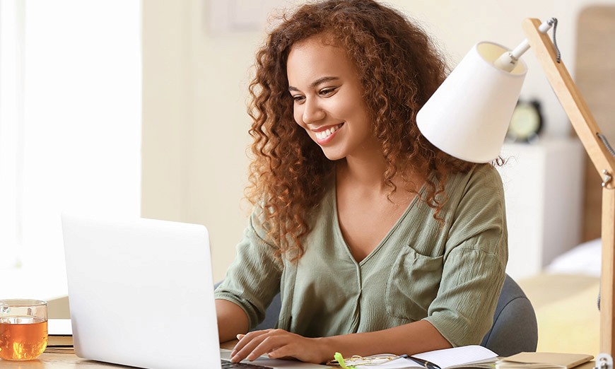 Woman smiling while typing on her computer, engaging with Pathroots article