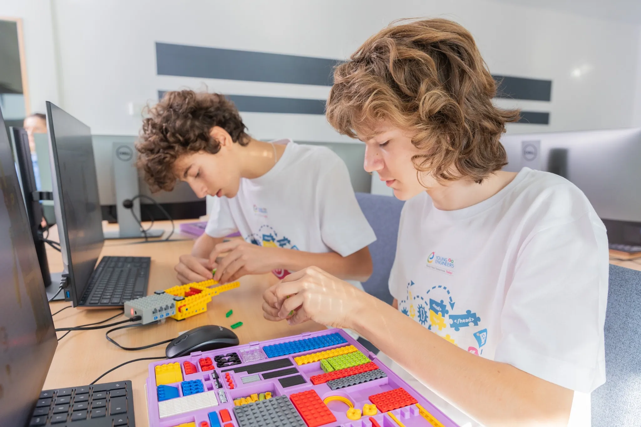Deux adolescents construisent un projet LEGO technique devant un ordinateur dans un atelier STEM.