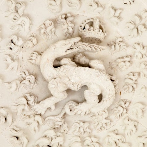 Un plafond voûté et orné avec des sculptures minutieuses, trois grandes fenêtres cintrées, et la lumière du soleil inondant une salle vide au sol en pierre.