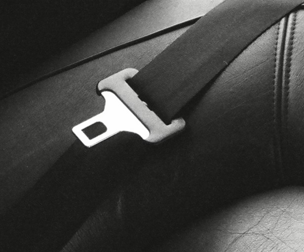 Close-up of a metal seatbelt buckle on a black seat, emphasizing safety in vehicles.