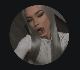 Confident woman with long curly hair wearing sunglasses and a shimmering top, photographed from a low angle against a deep blue sky.