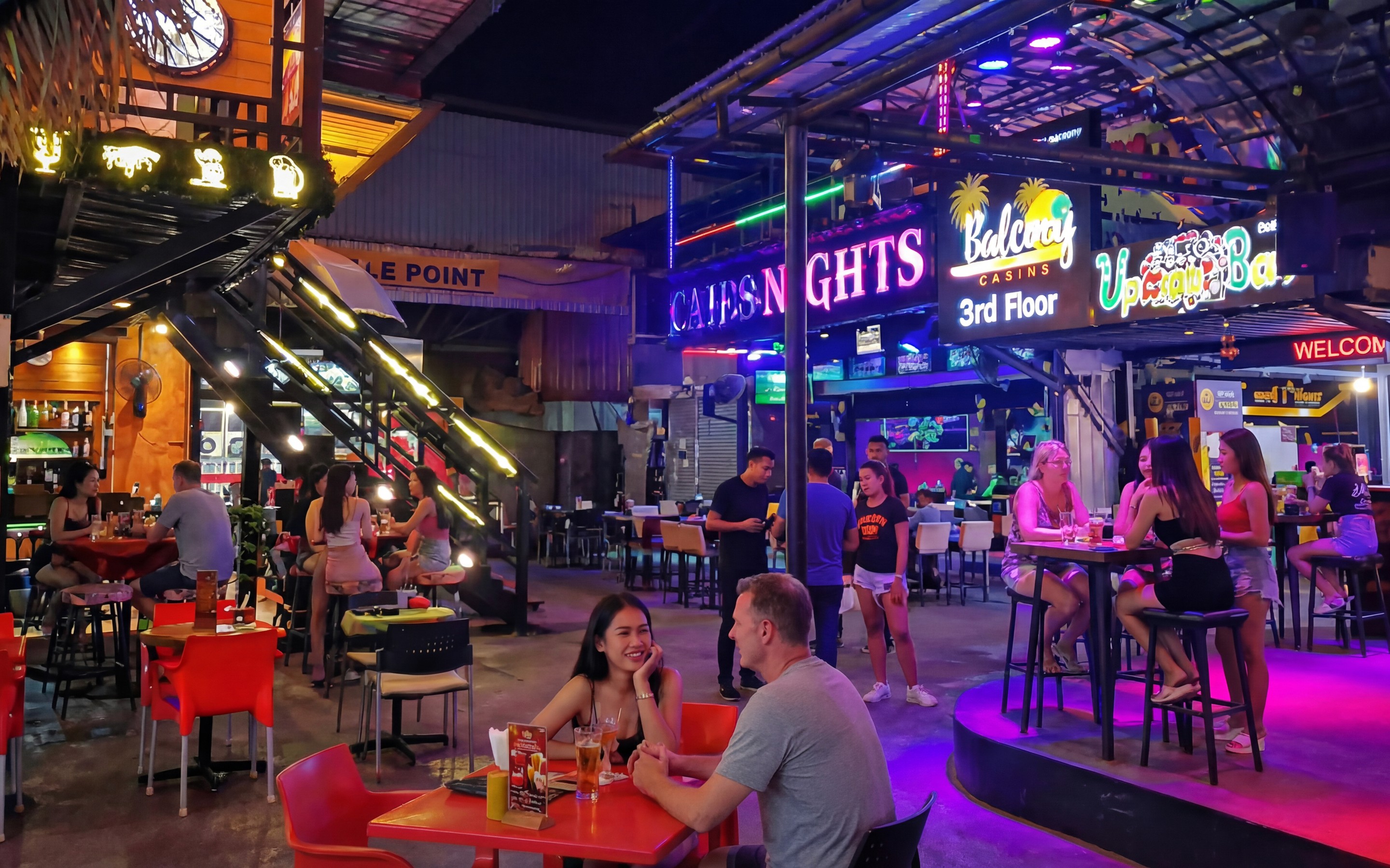 Evening street scene in Ao Nang’s nightlife area with bars, neon signs, and people seated at tables.