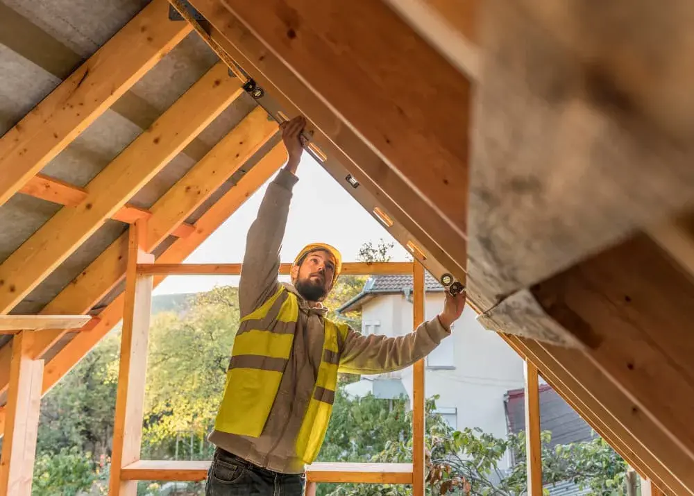 A construction worker in a reflective vest uses a level tool while working on a house frame. The image represents progress, precision, and the hands-on process of building a new home—reflecting the care and support offered through Chris Lewis Home Loans' construction financing.