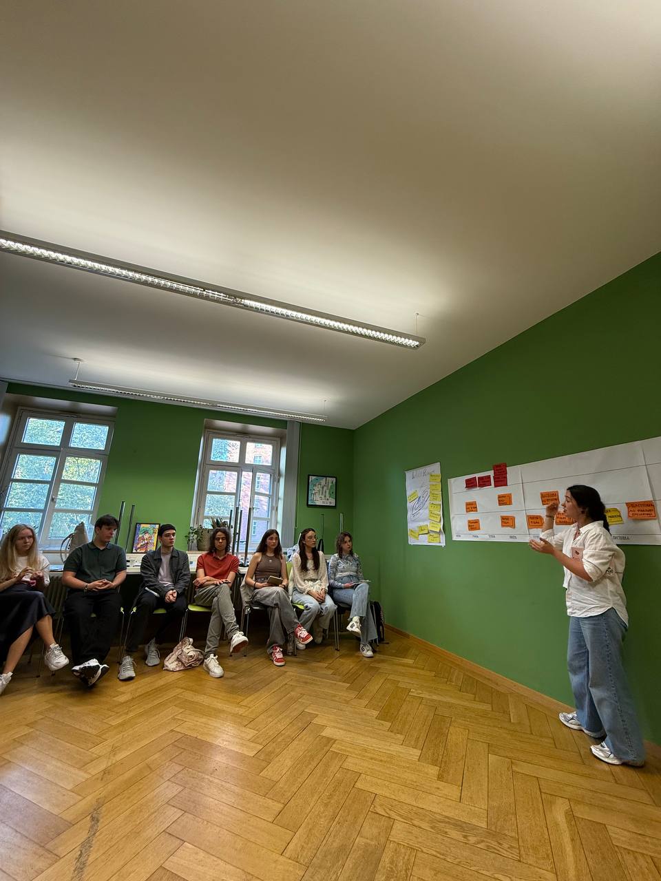 Junge Menschen sitzen auf Sofas und hören aufmerksam einem Workshop zu.