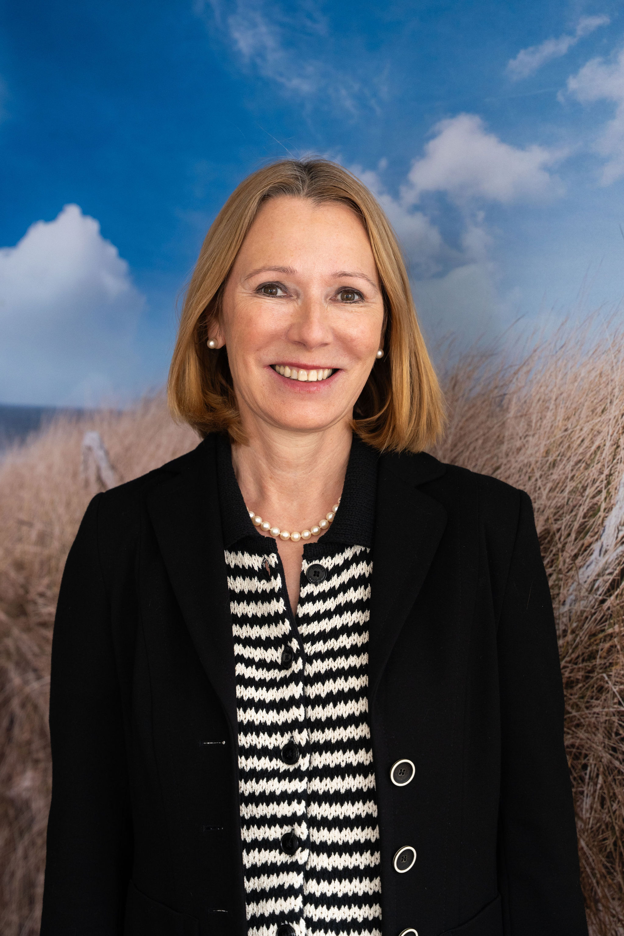 Woman in a blue shirt poses confidently with folded arms, wearing glasses and jewelry. Neon lighting casts a purple and pink glow, creating a vibrant mood.