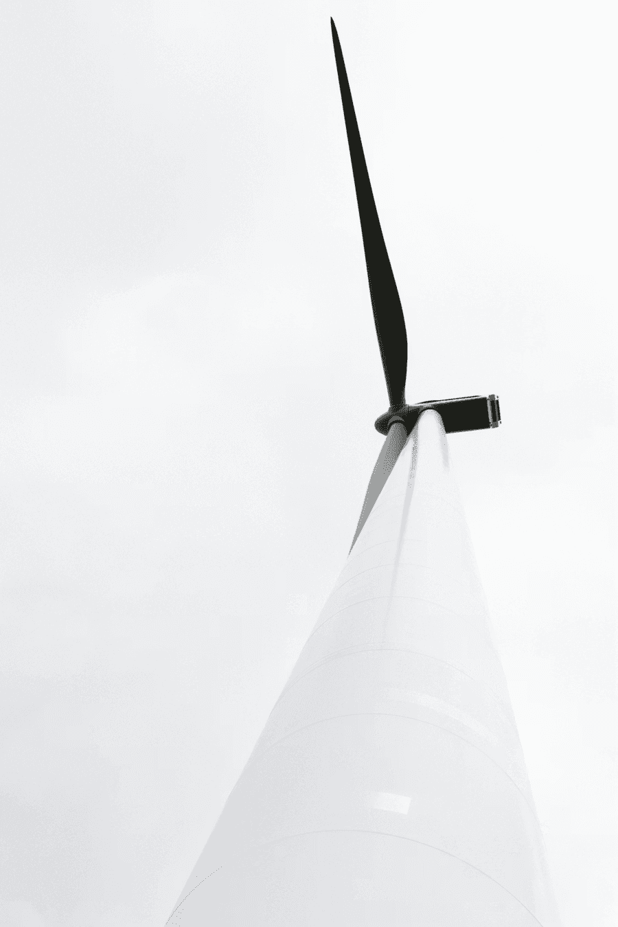 Close-up view of a wind turbine blade against a pale sky, representing renewable energy.