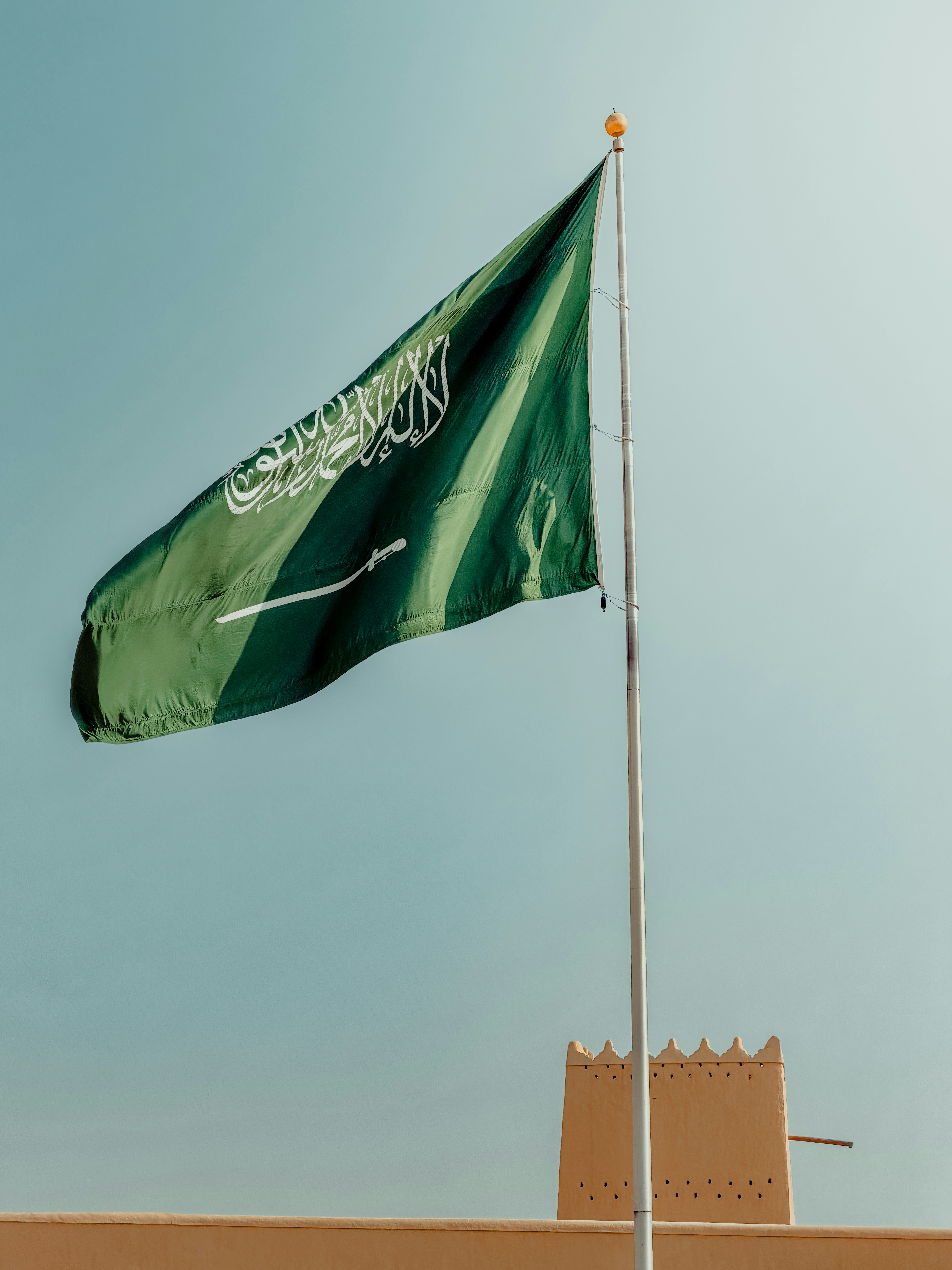 Saudi arabian flag waving against a clear blue sky.