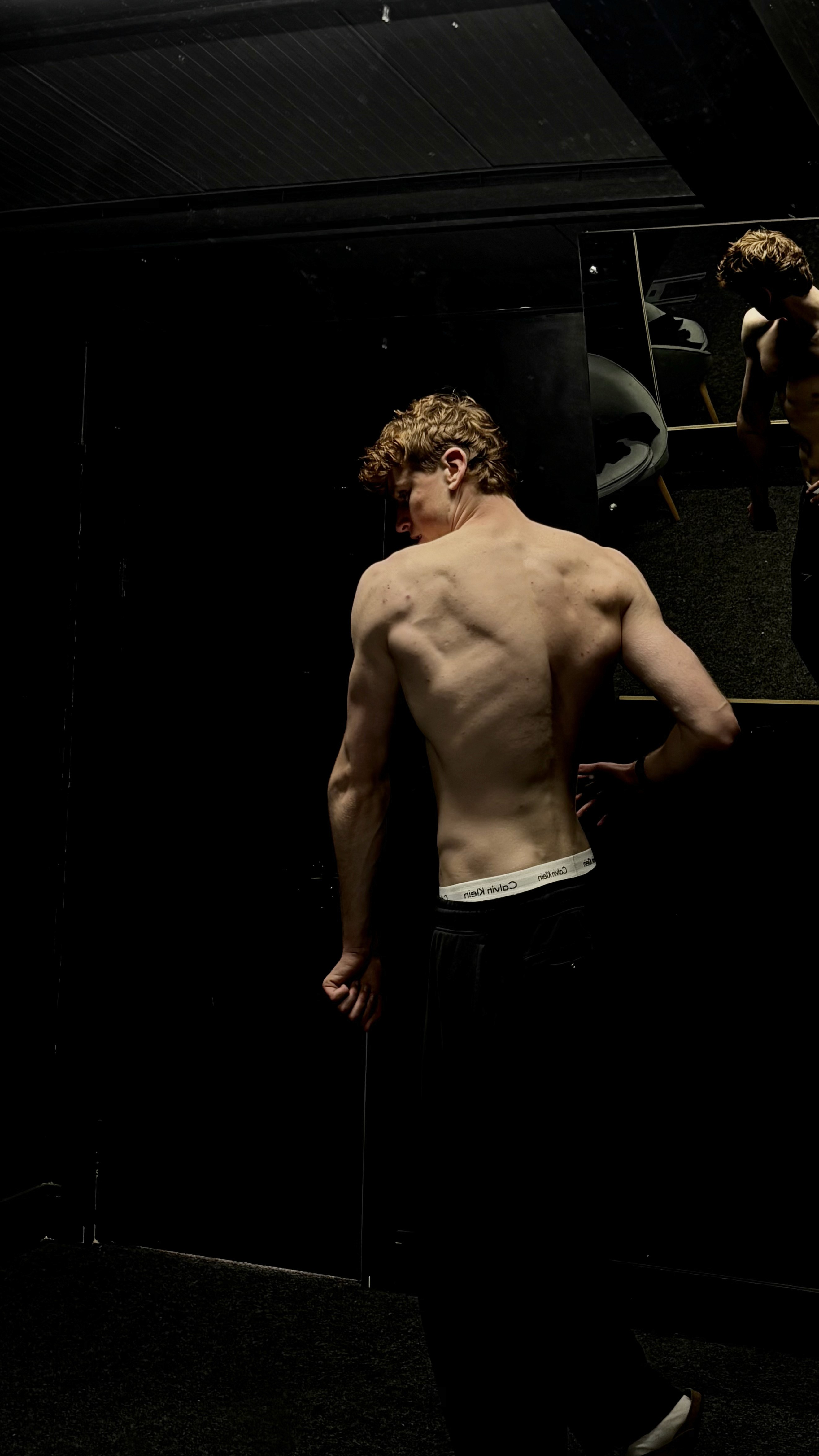 jesse showing back physique development in a dark gym