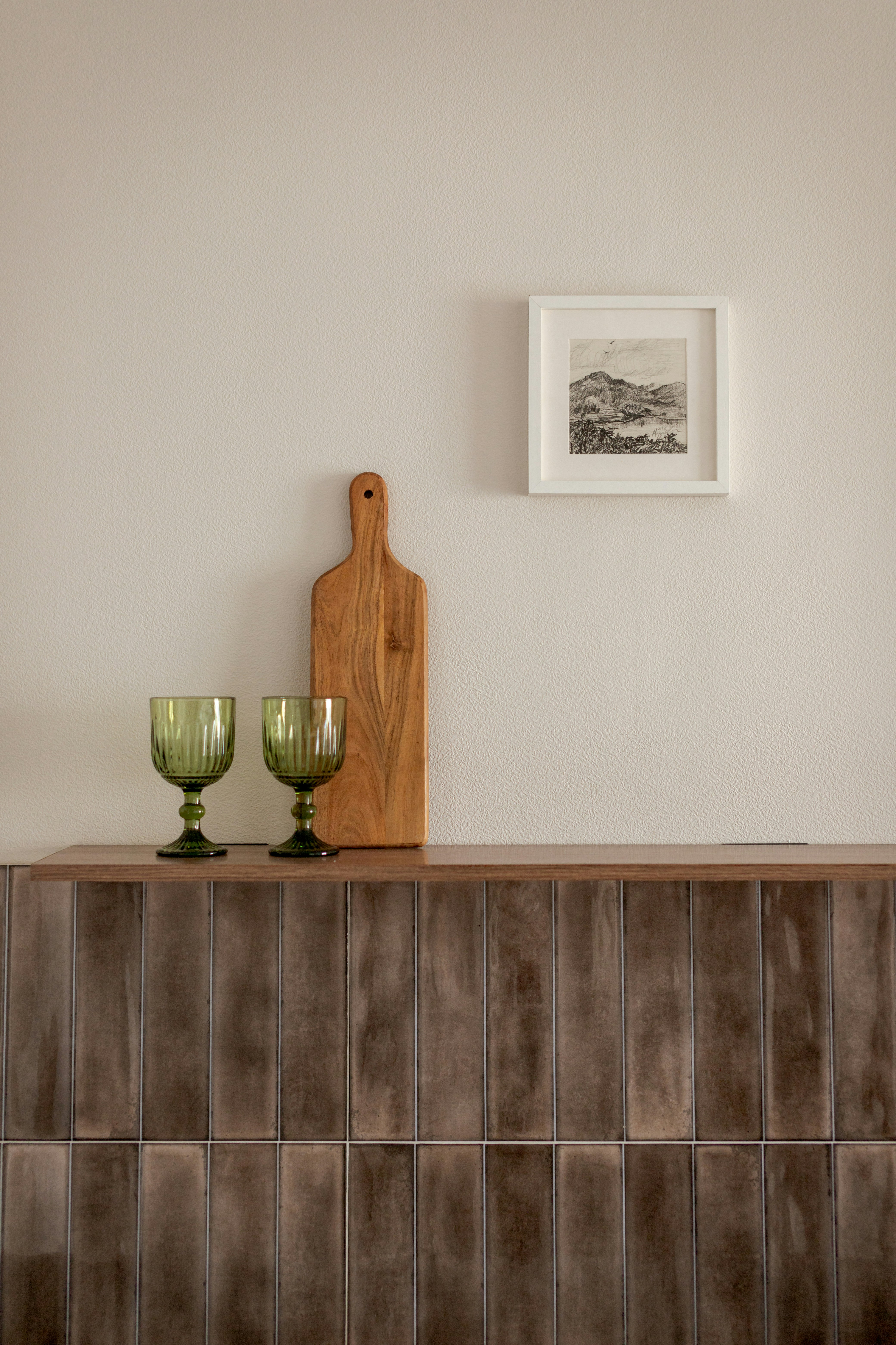 Two green glasses and wooden cutting board on shelf.