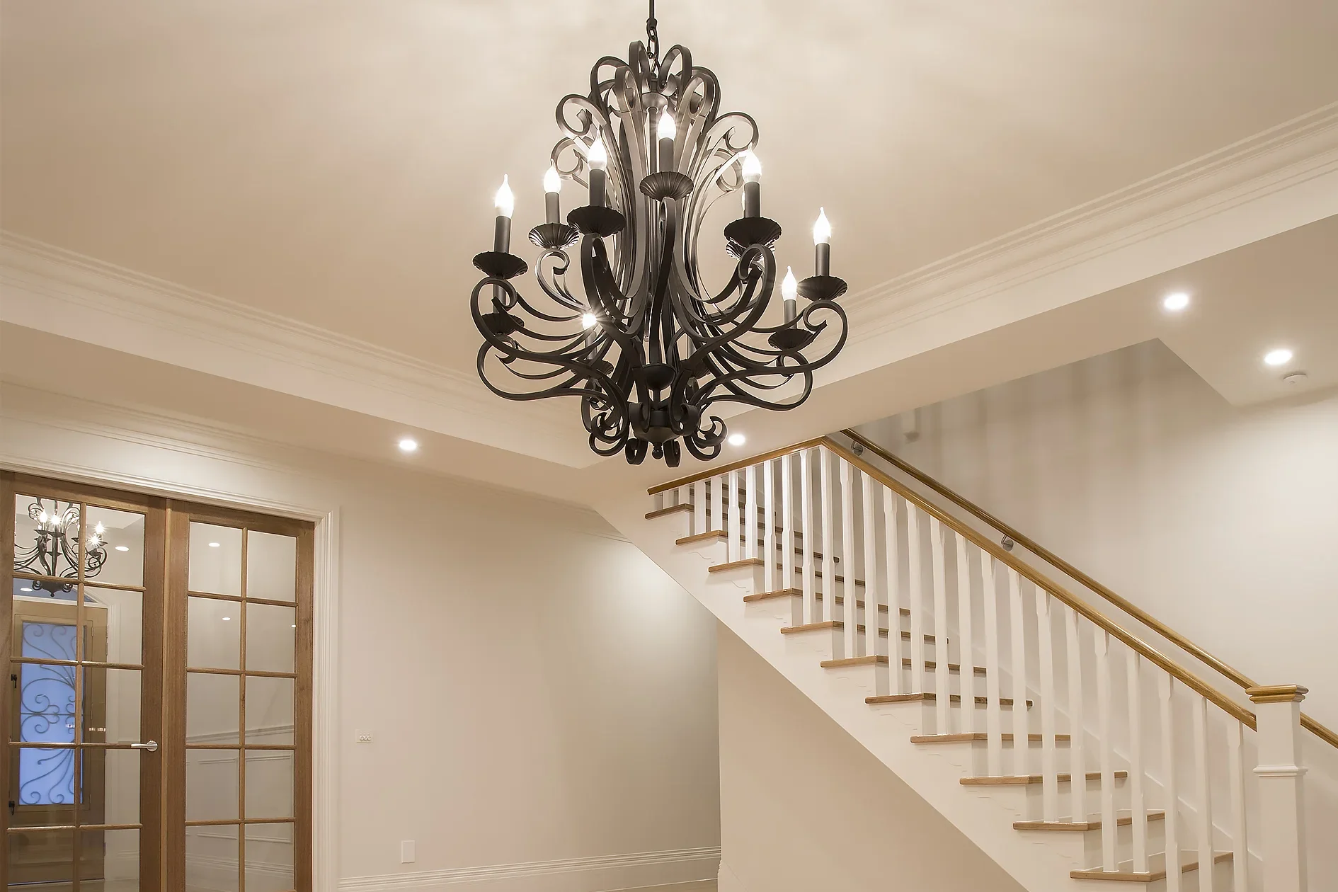 Entry foyer of Plenty Residence with an ornate black wrought-iron chandelier and a white timber staircase with oak handrail