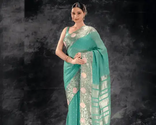 A woman wearing a teal blue georgette saree with shimmering golden borders from That Saree Shop, showcasing the saree’s lightweight flow and graceful, festive elegance.