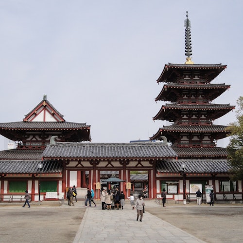 人们走在一座拥有多层塔楼和传统建筑的历史悠久的日本寺庙前。