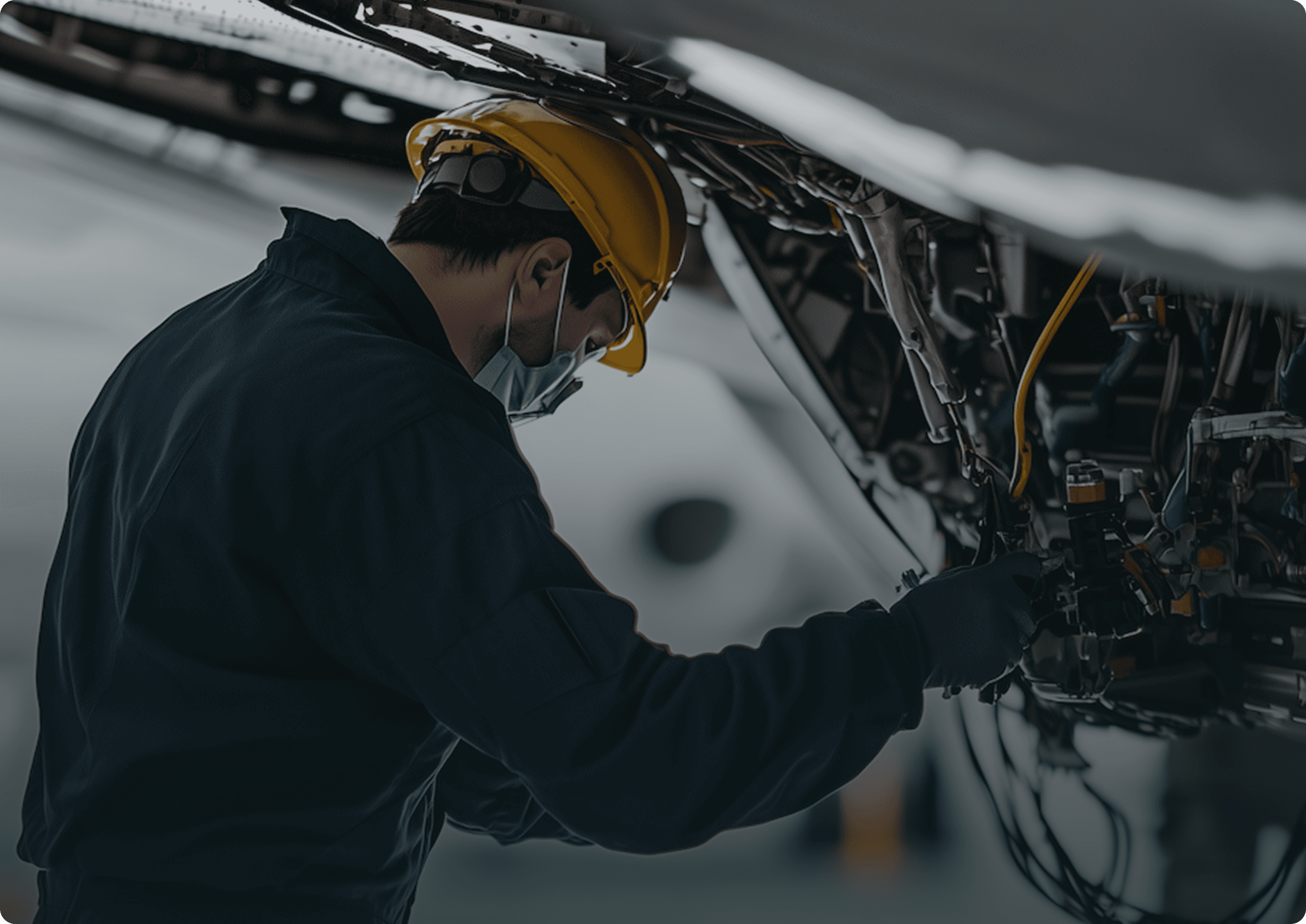 Electrician in a hard hat and face mask working on wiring inside industrial equipment