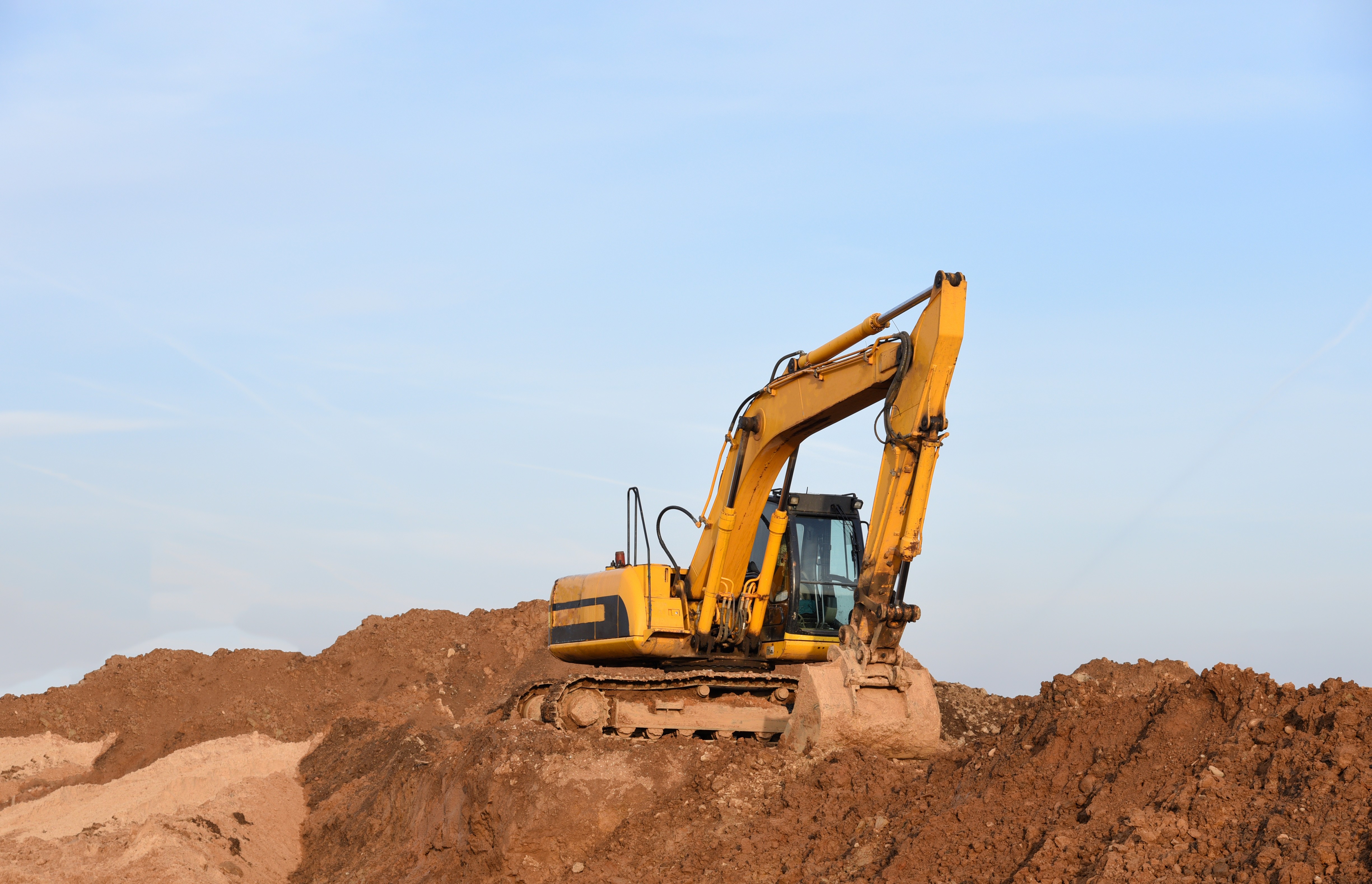 Yellow excavator positioned on a mound of soil at a gold mining site, ready for earthmoving operations against a clear blue sky.