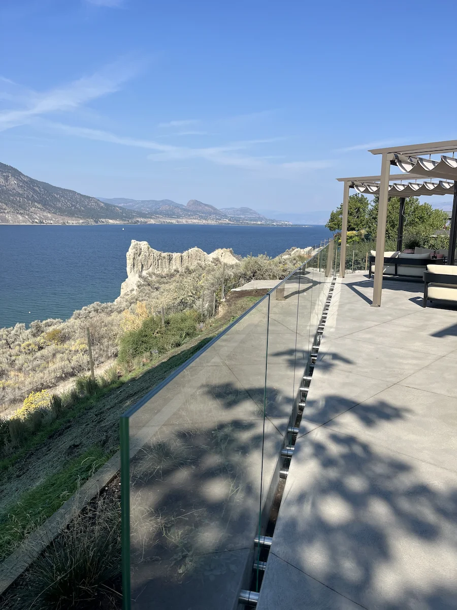 Frameless glass railing along a modern patio overlooking ocean cliffs and blue water, offering clear panoramic coastal views in British Columbia.