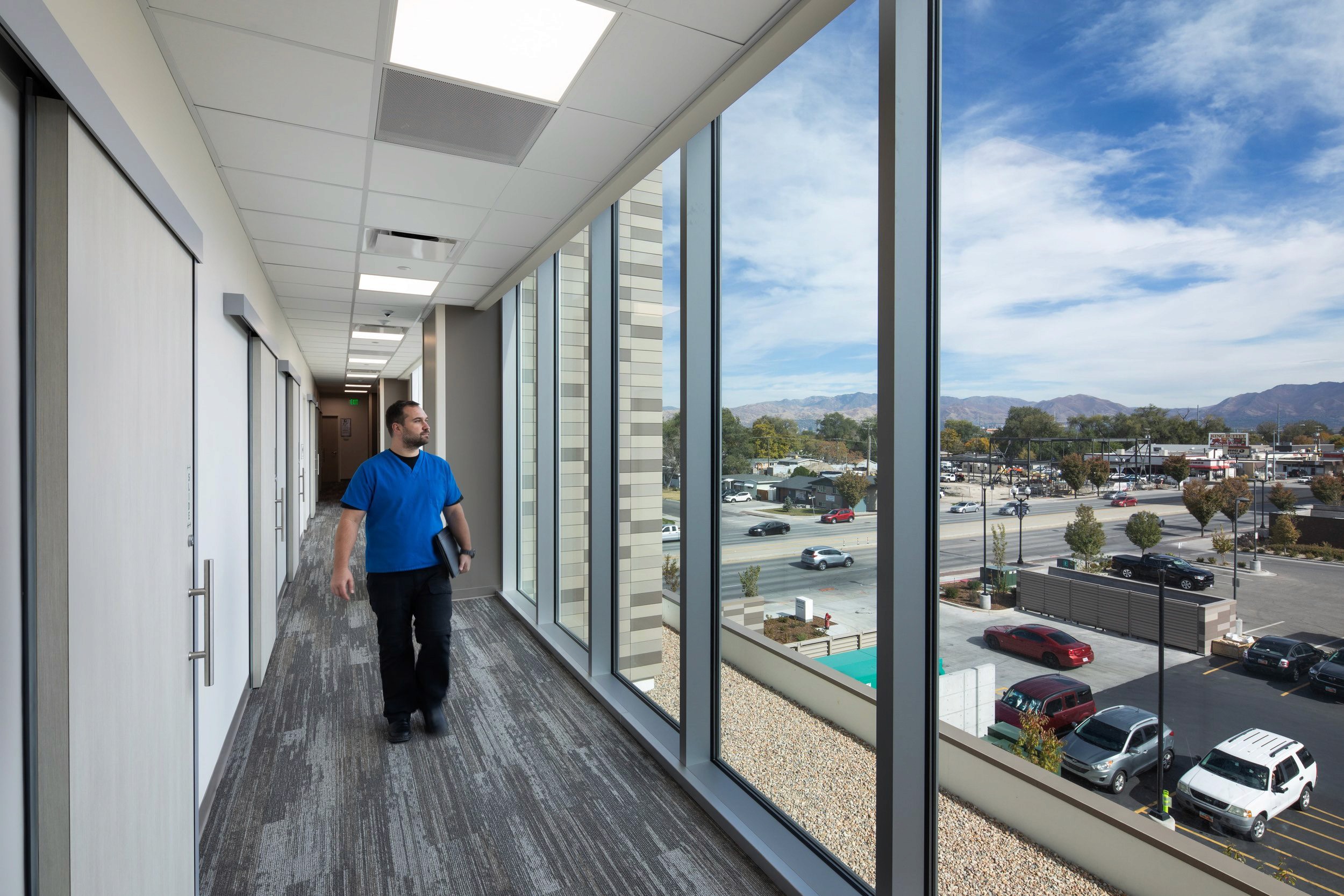 Man walking down a modern hallway with large windows.