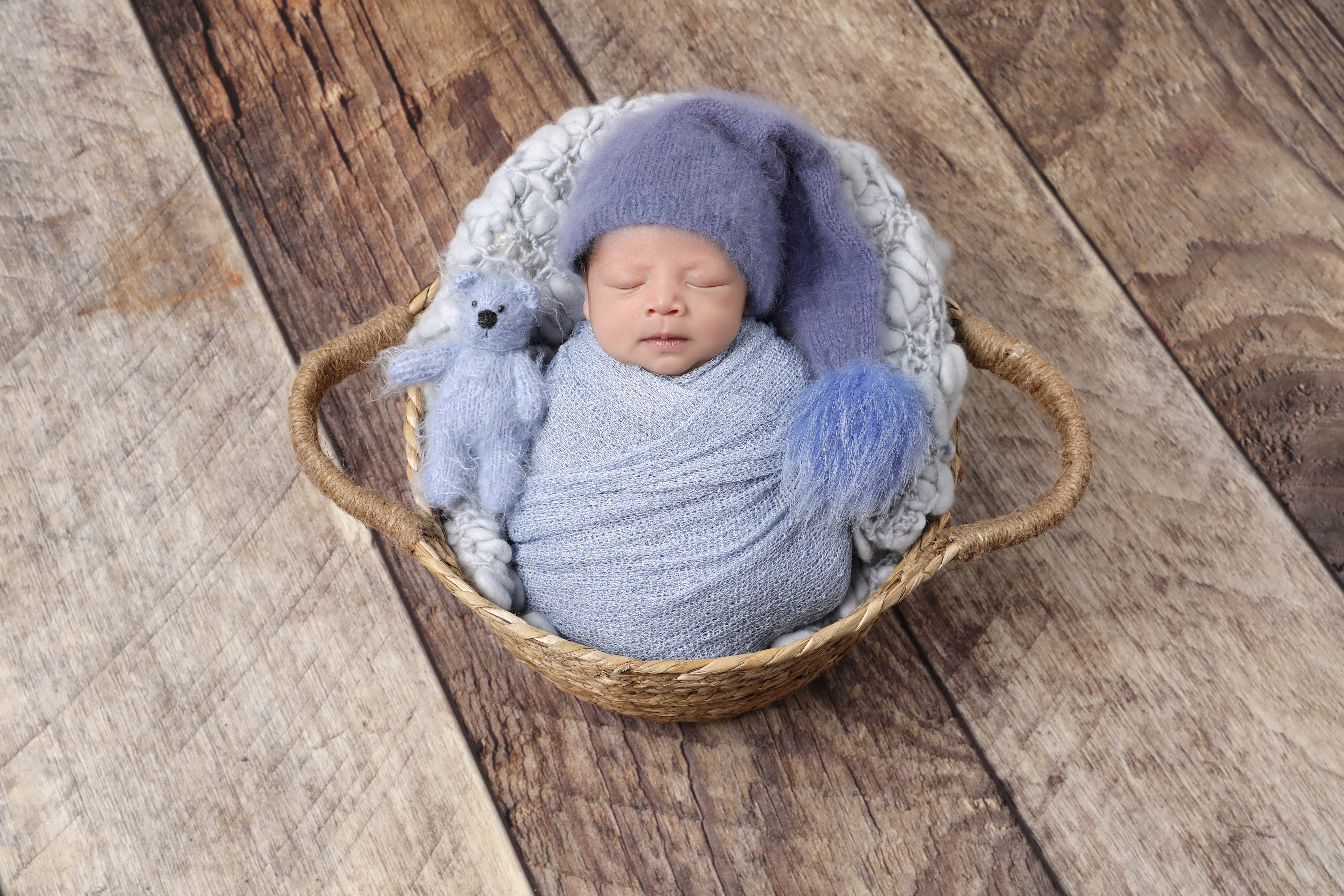 Newborn baby boy wrapped in blue blanket while lying in a basket.