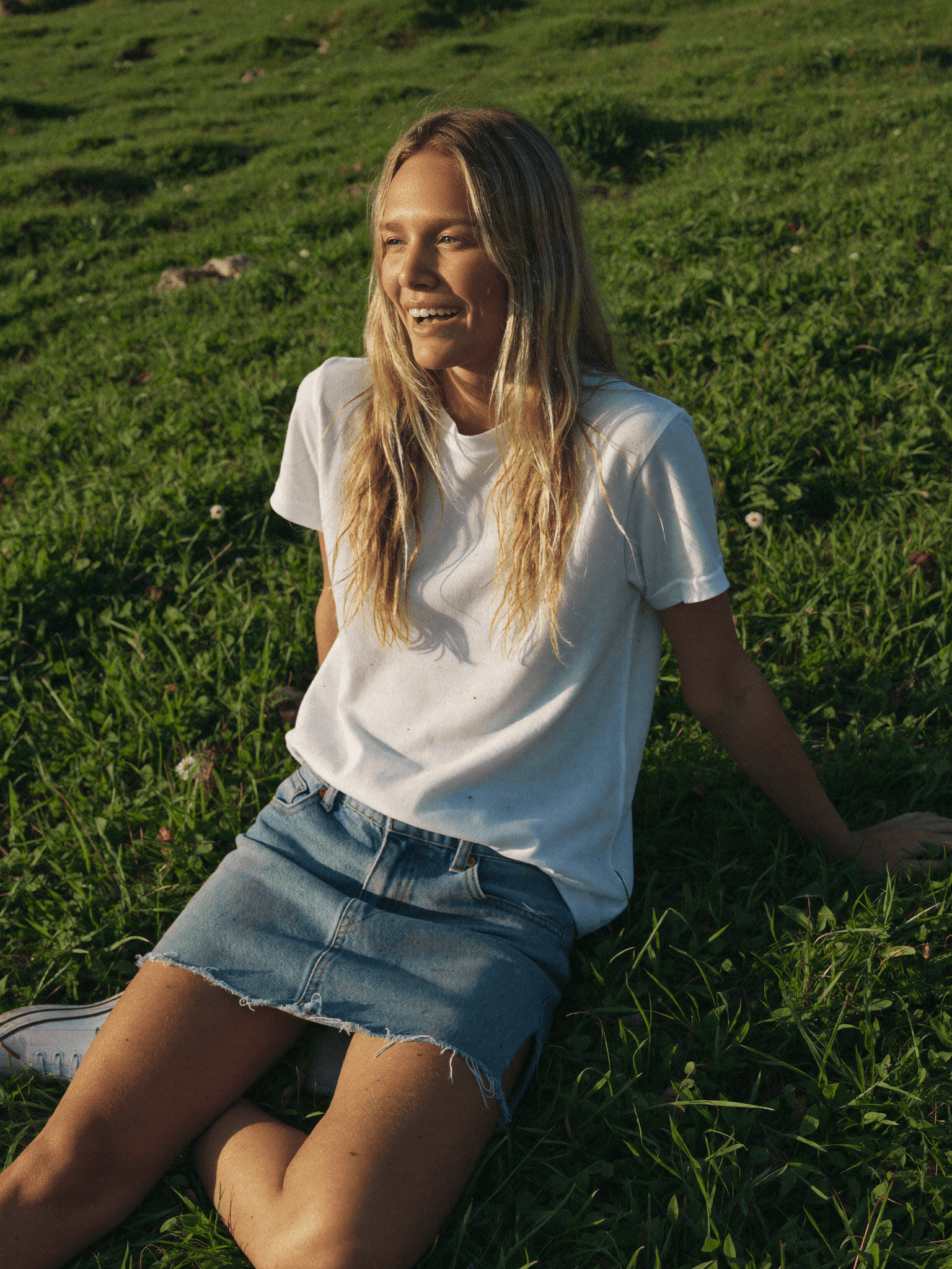 Close-up of Mia Wald resting in green grass, looking toward the camera in warm afternoon sunlight.