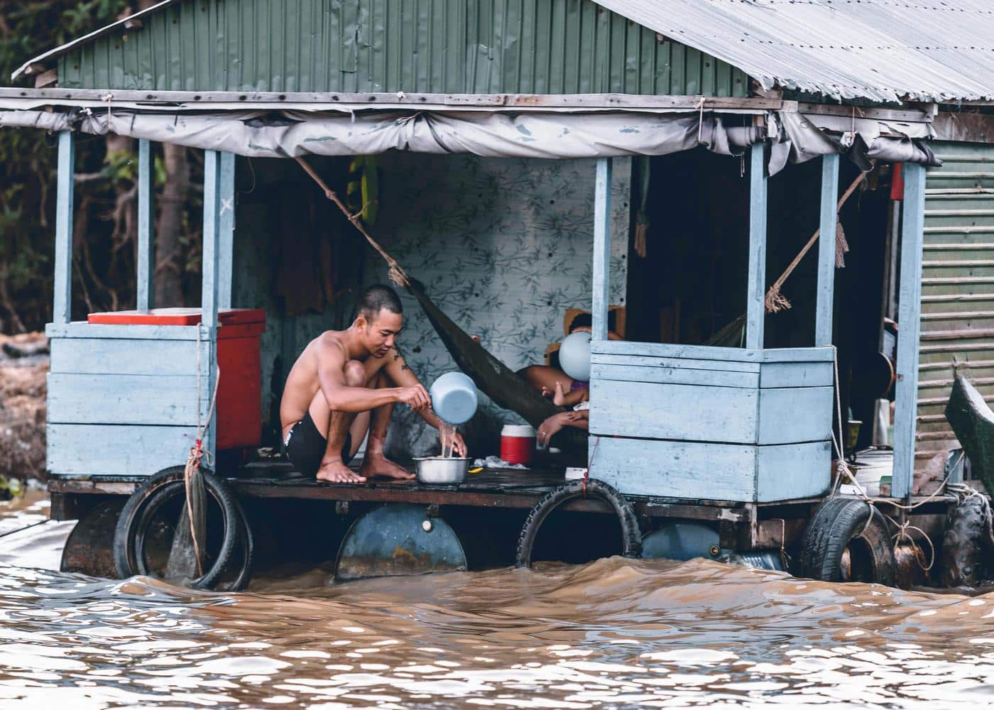 Man taking water from the floodwater running past his house