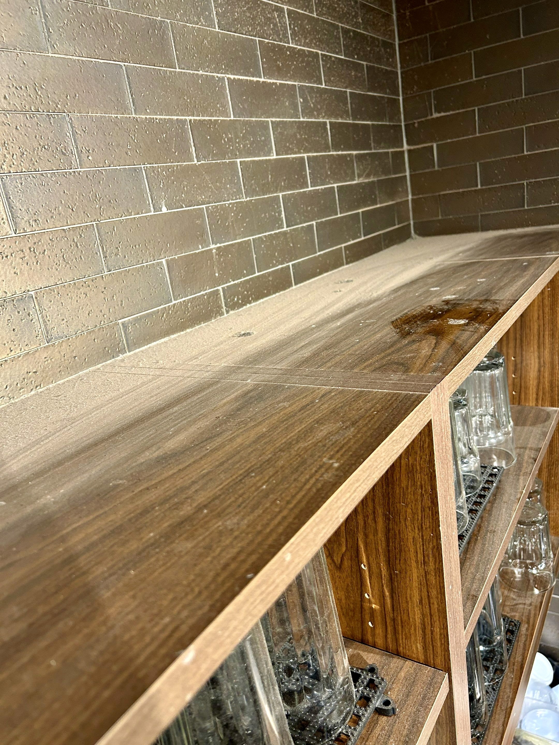 Thick dust accumulation on wood shelving above bar area.