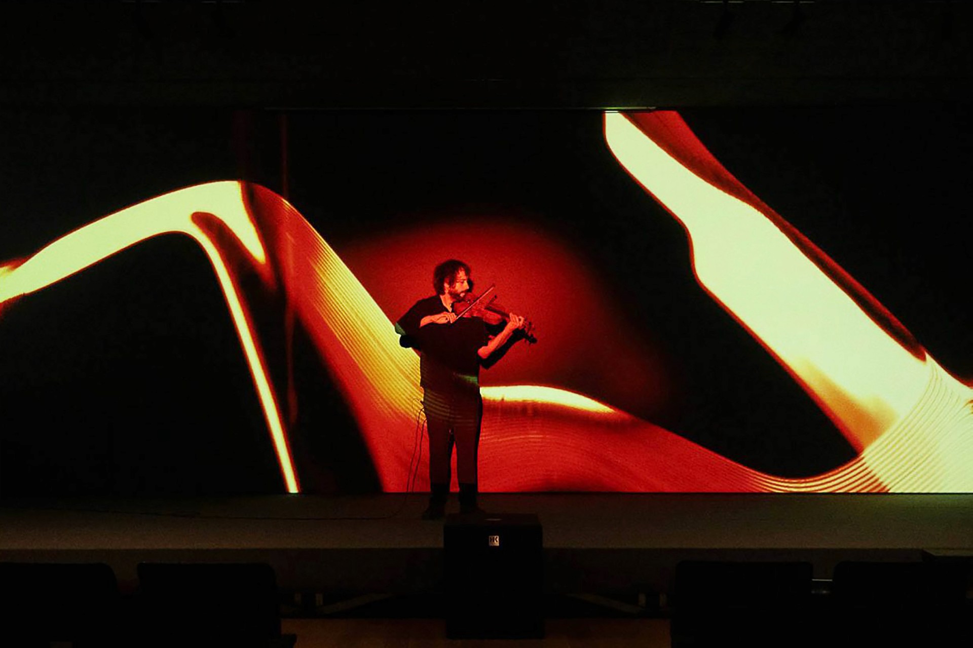 Man playing the violin with a projection of an abstract ochre-coloured organic form