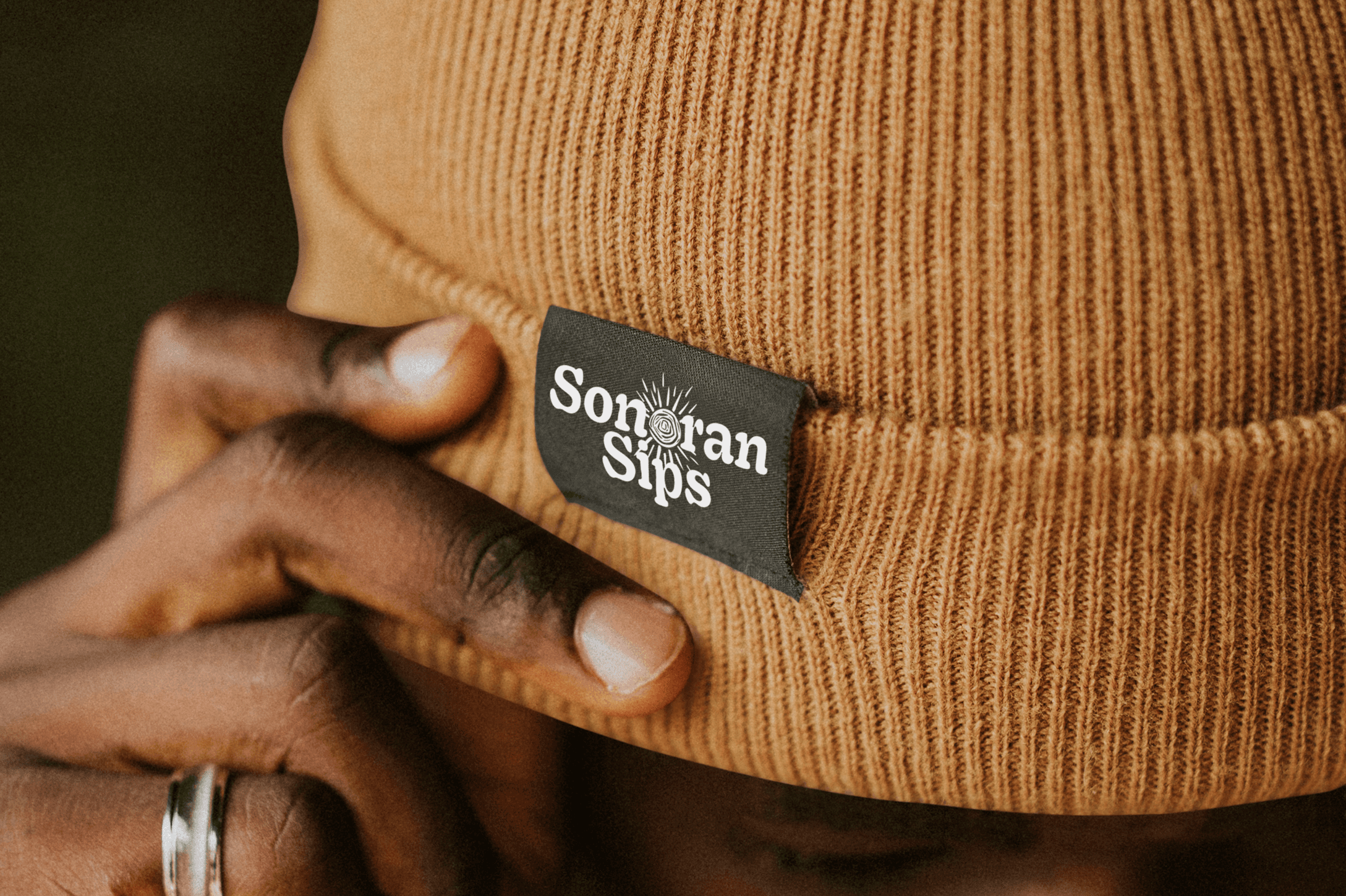 Photo of a man holding the side of his beanie with "sonoran sips" logo tag on the side