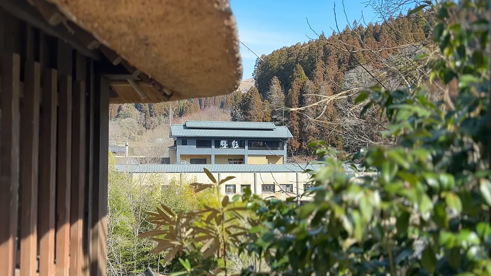 A thatched eave at Kurokawa Onsen framing a white inn across the valley