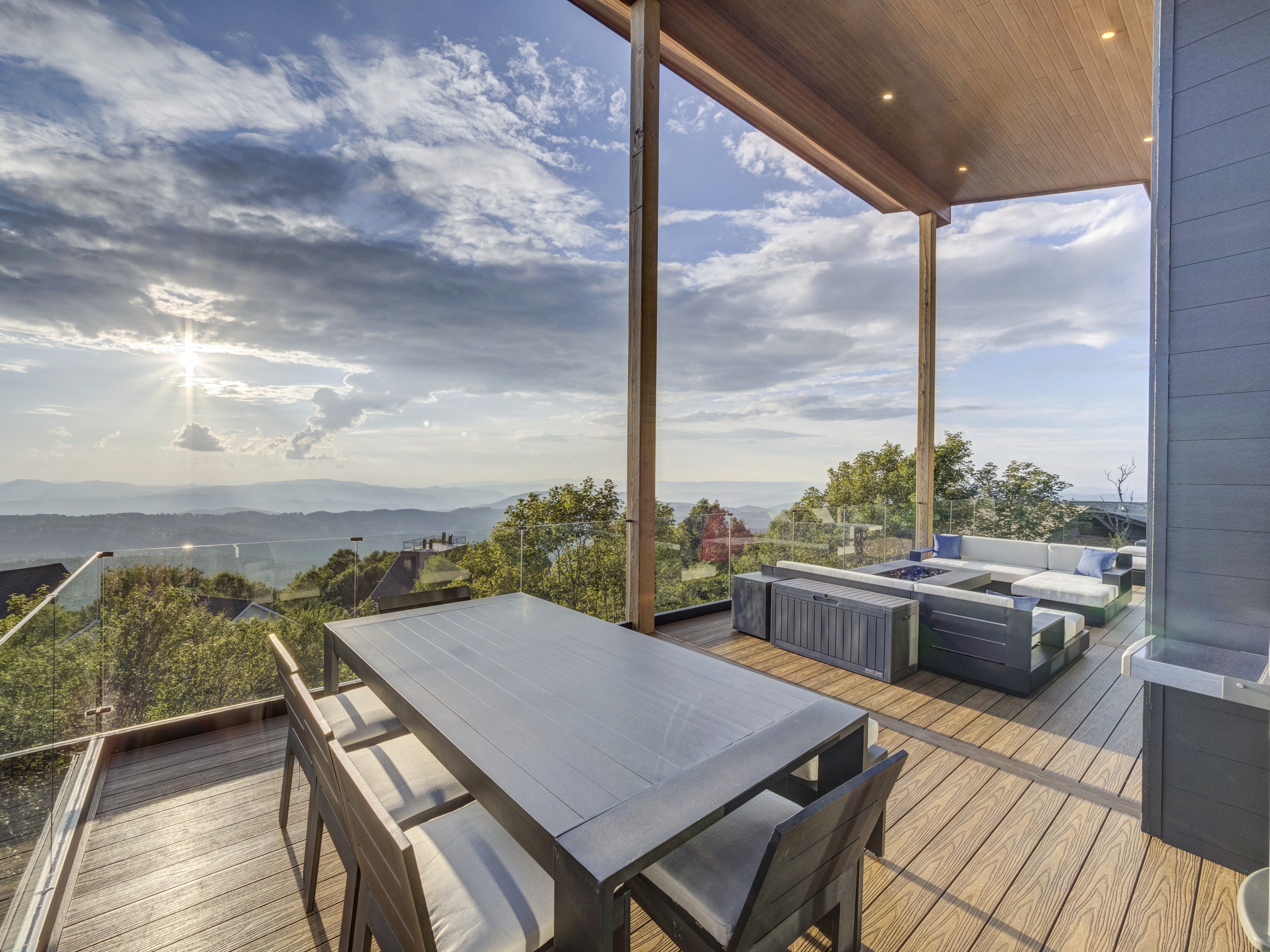 Luxury modern wooden deck at sunset with a contemporary dining set and glass railings overlooking the mountains