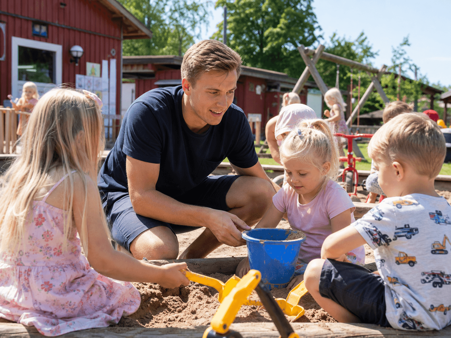 En barnehagevikar fra Leo Bemanning leker i sandkassen med barna, som illustrerer trygg lek og aktivitet med sommer- og ferievikarer.