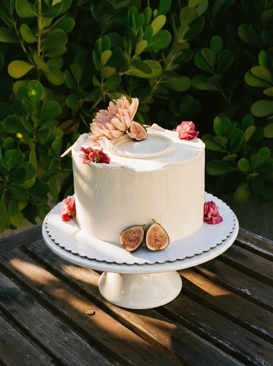 Wooden outdoor table set with multiple plates of food, including dips, salads, potatoes with cheese, and glasses of water, with hands reaching in to eat.