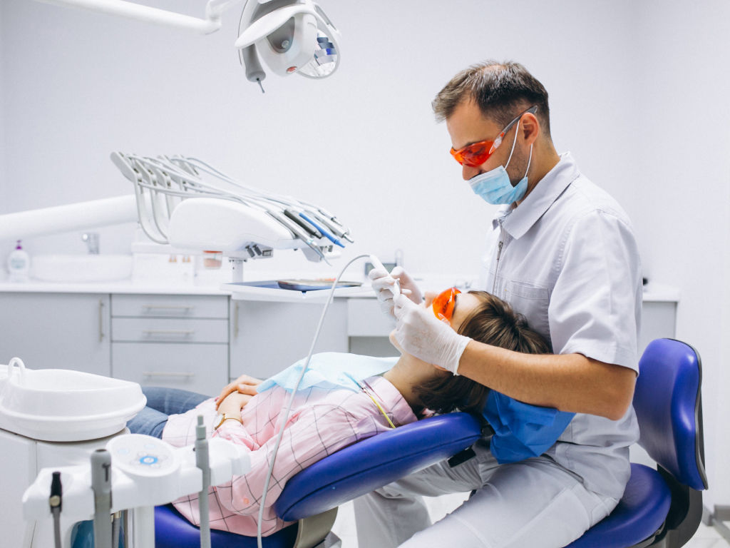 A man and woman sitting in a dental chair, receiving dental treatment from a dentist and dental assistant.