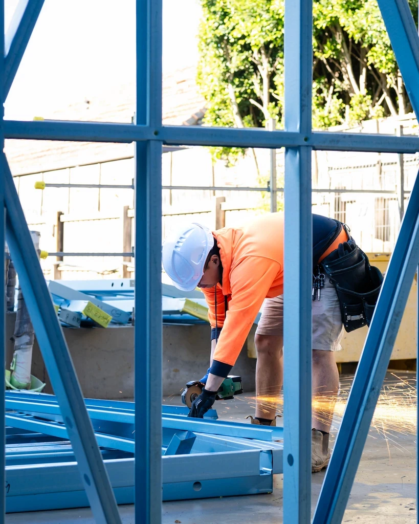 Construction worker cutting steel beams with power tool on-site.