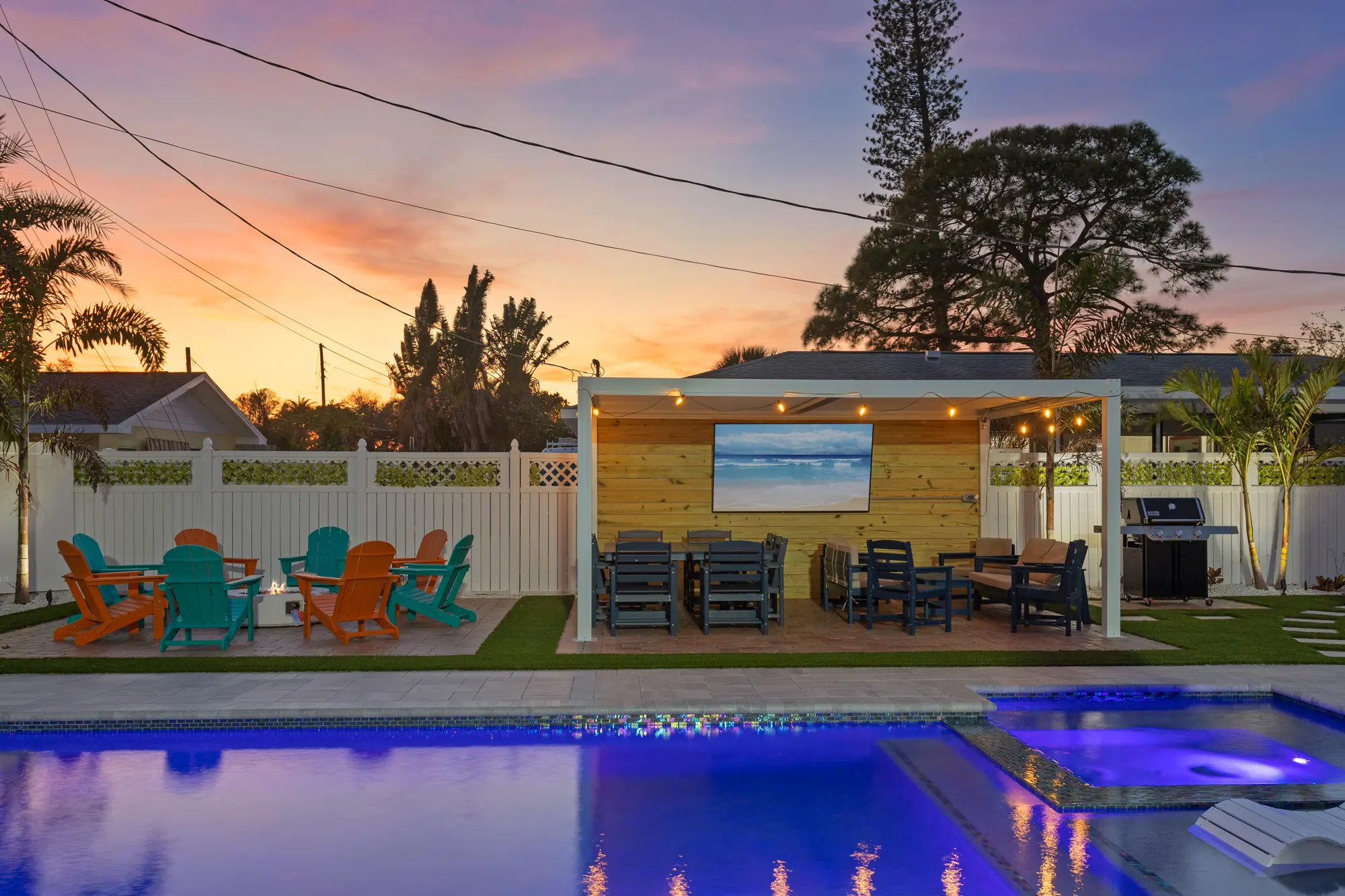 Covered pavilion with dining tables and an outdoor TV beside the lit pool and hot tub at sunset at Pickleball Resort, Bradenton, Florida