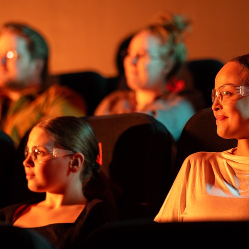 A girl and her mother watch the Lava Show. They are wearing safety goggle. Other people are in the background.