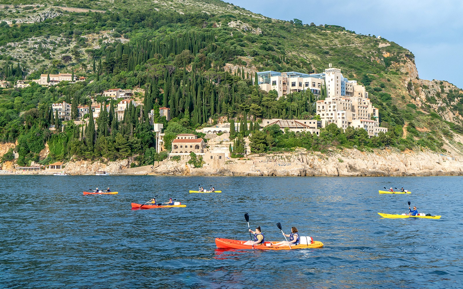 Kayakers paddling near Dubrovnik's coastline with lush hills in the background.