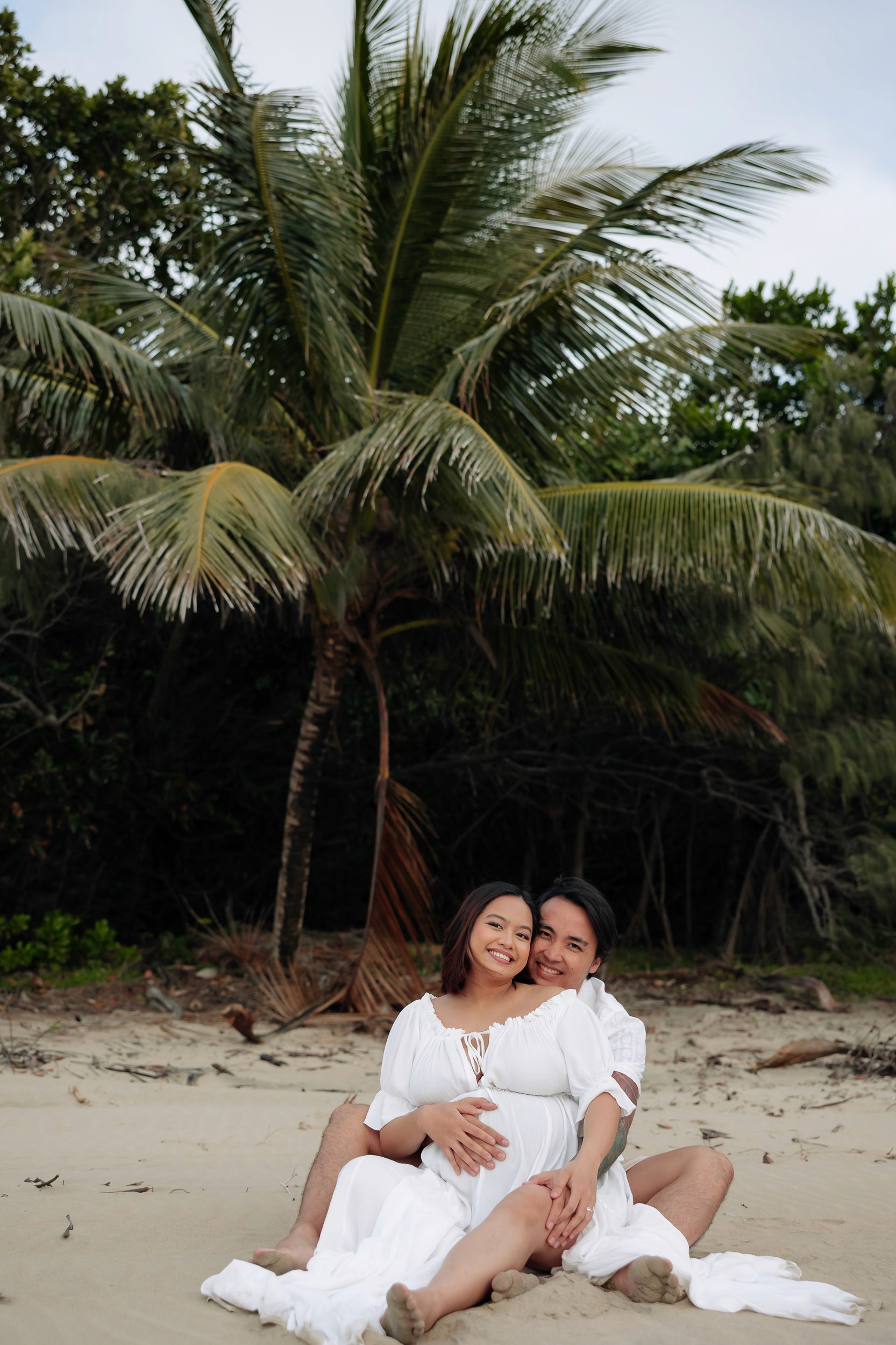 Expecting couple sitting on the sand cuddling