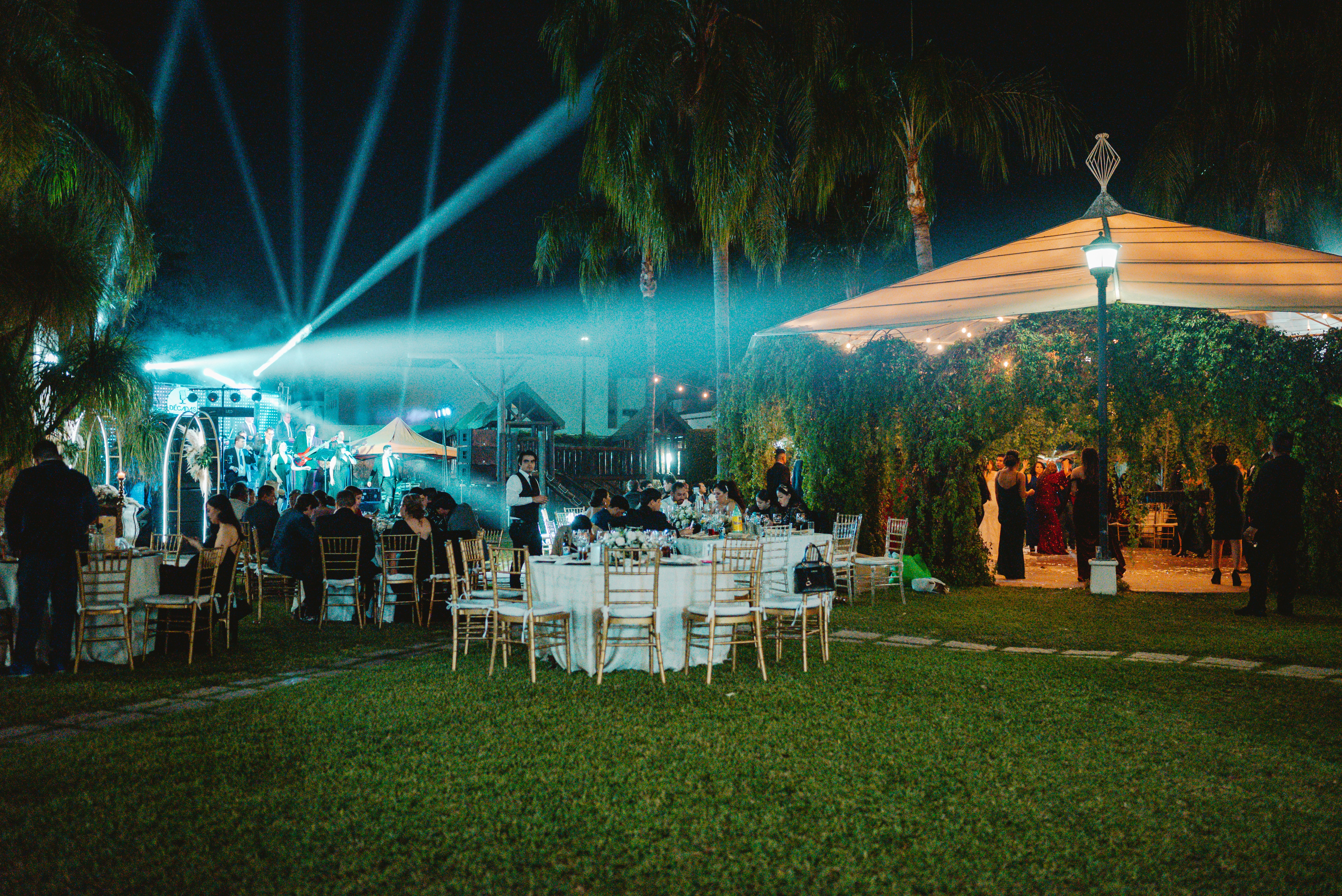 Outdoor event with illuminated tables and guests at night.