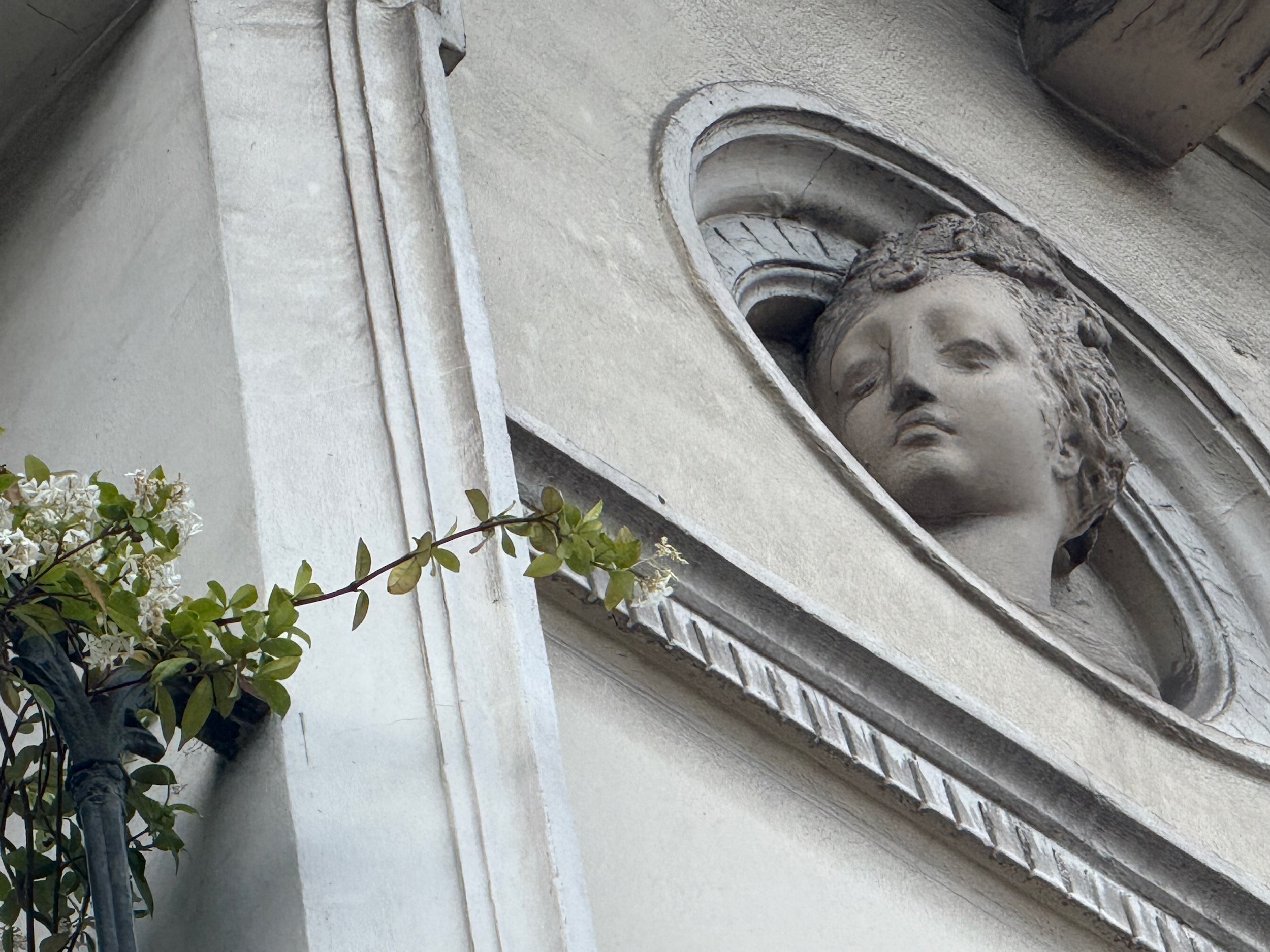A carved stone face of a woman looks out from an oval niche on a Paris building.