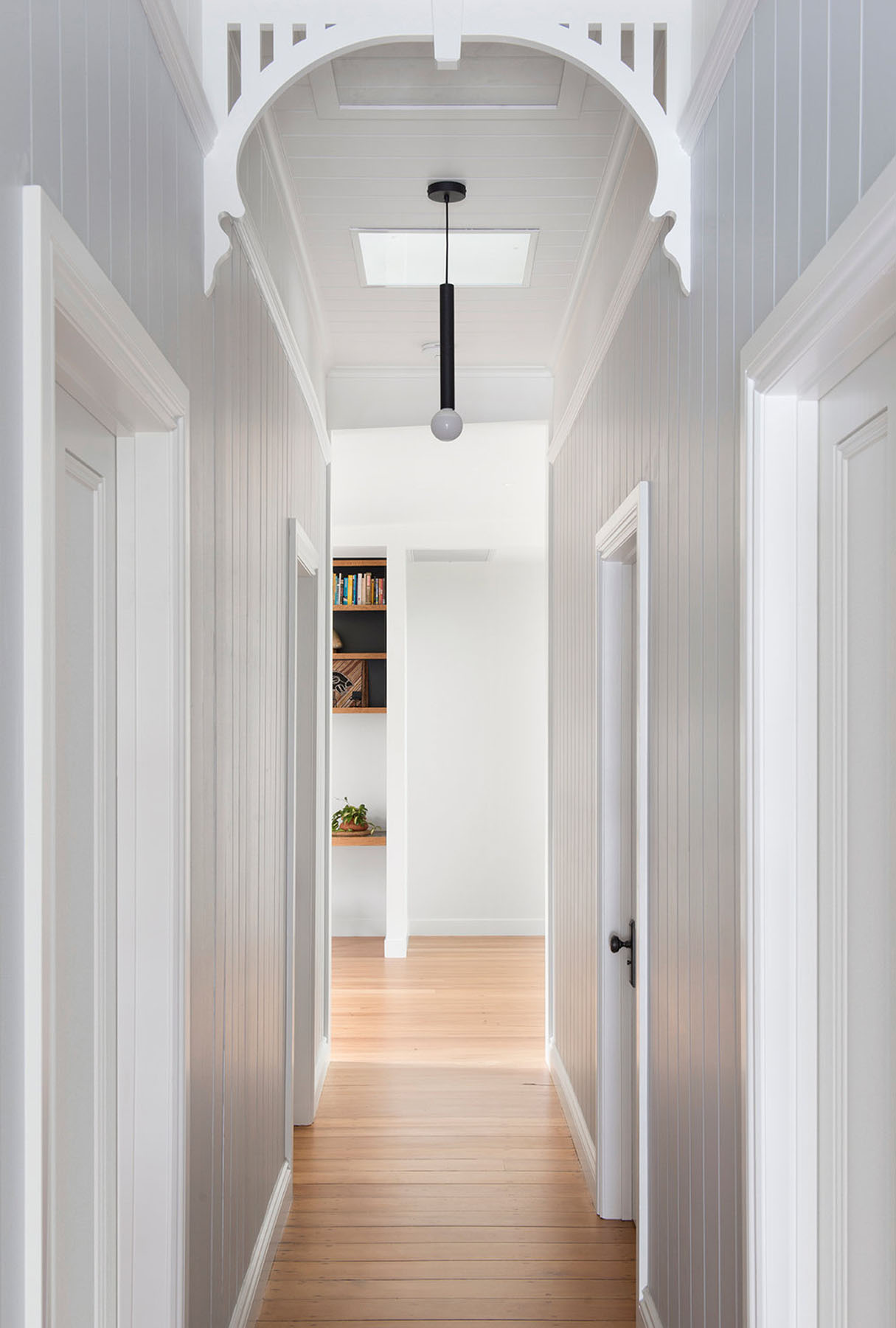 Original hallway with decorative arch, vertical lining boards, and a restrained monochrome palette.