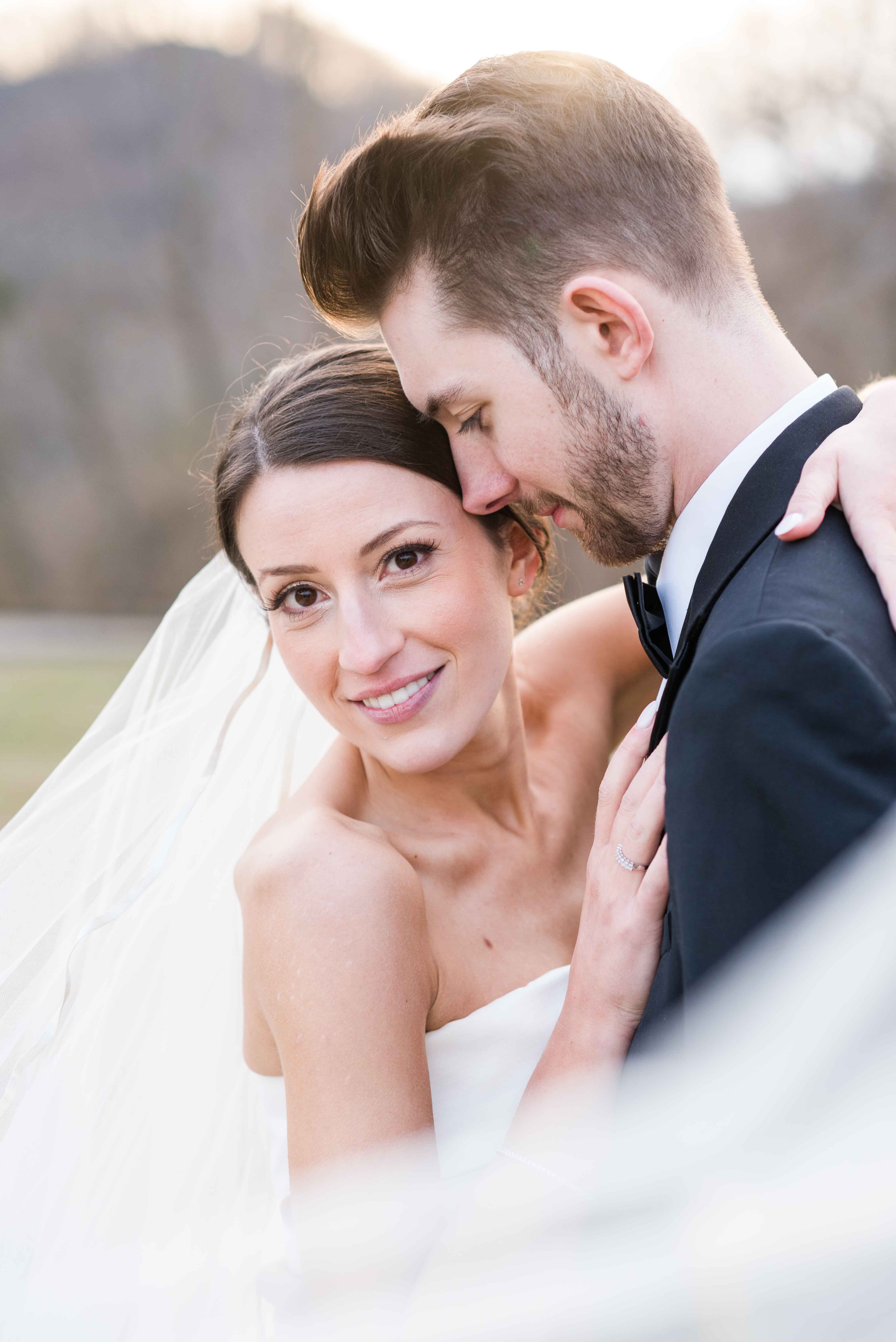 Portrait of bride and groom close up on their wedding day, bride is looking at camera, groom is looking down at his bride.