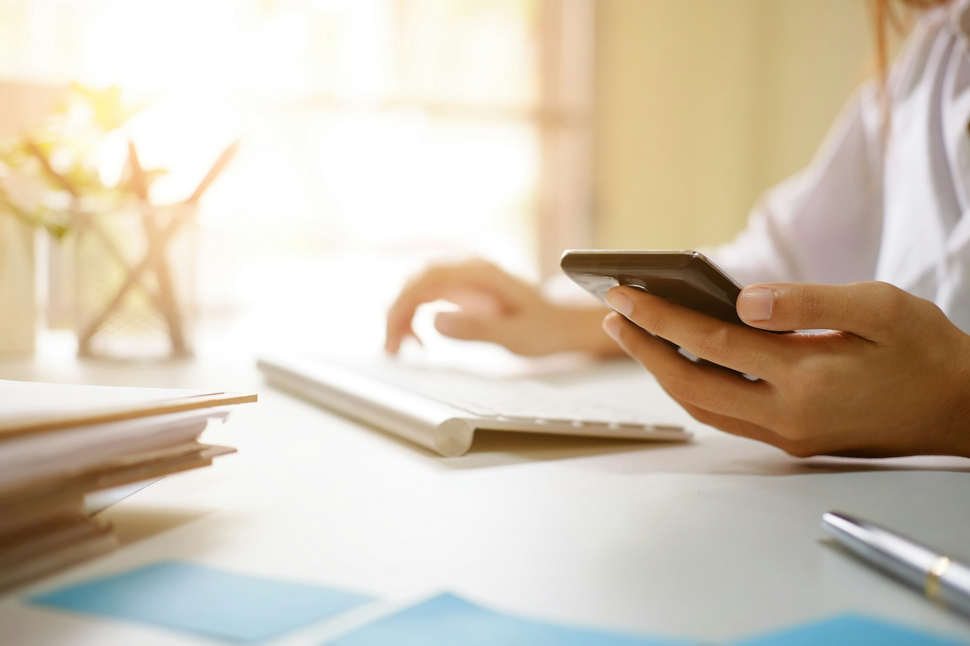 A person holding a phone while typing to a keyboard
