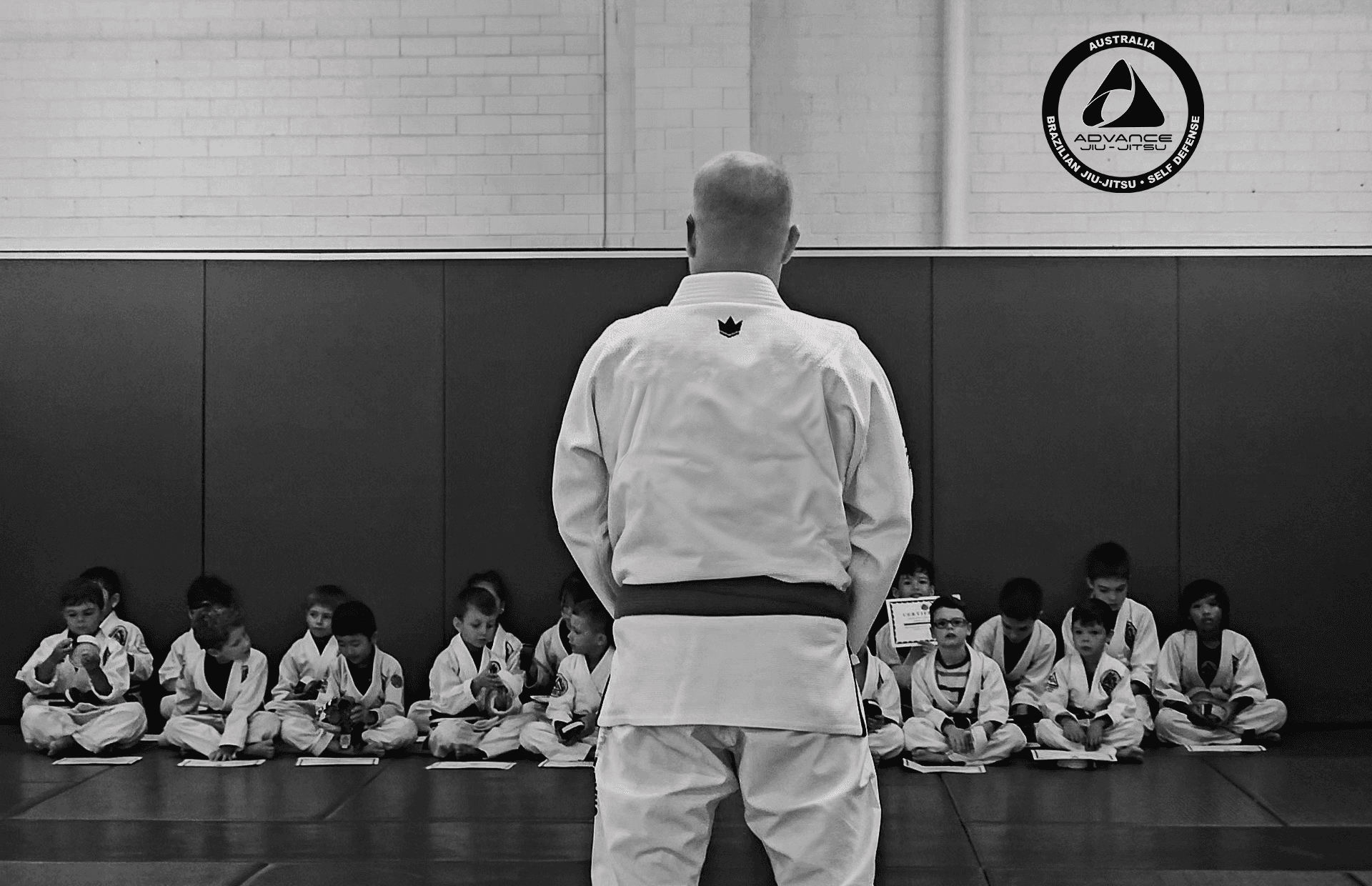 Instructor with Gracie Sydney patch on back addressing seated students in a gym setting