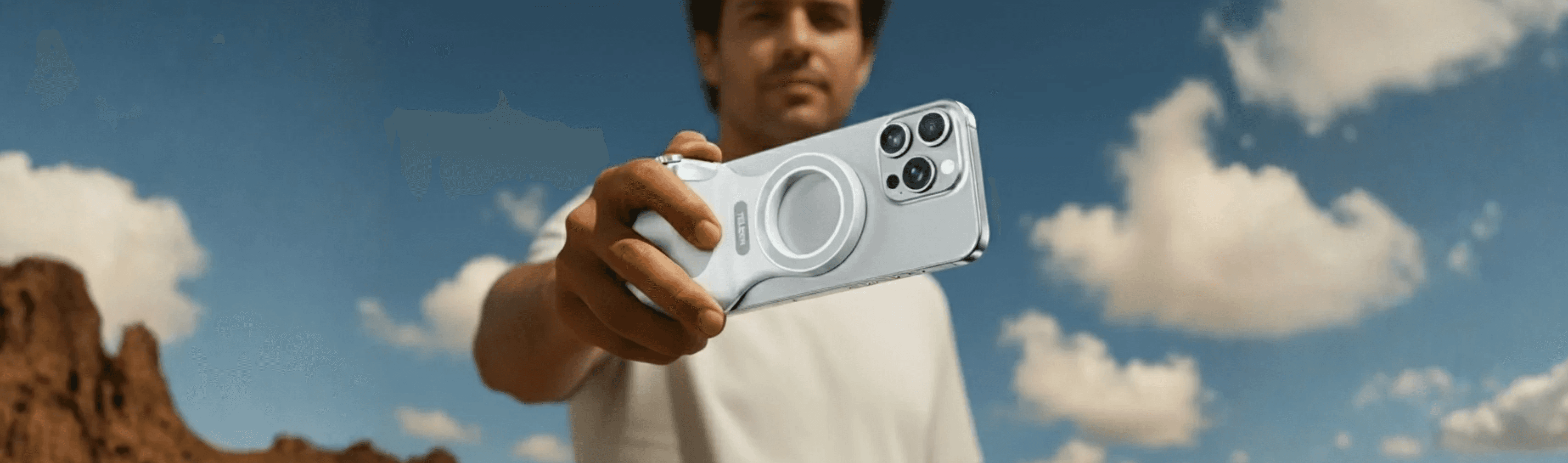 Athletic man in a sleeveless black outfit posing confidently outdoors under a bright blue sky, with a close-up of navy and salmon-colored men’s running shoes in the foreground.