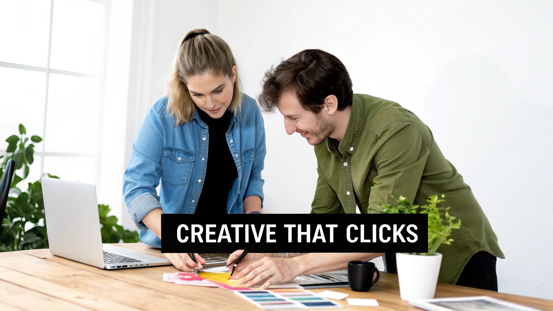 Two smiling designers collaborate on color swatches and designs at a wooden desk with a laptop.