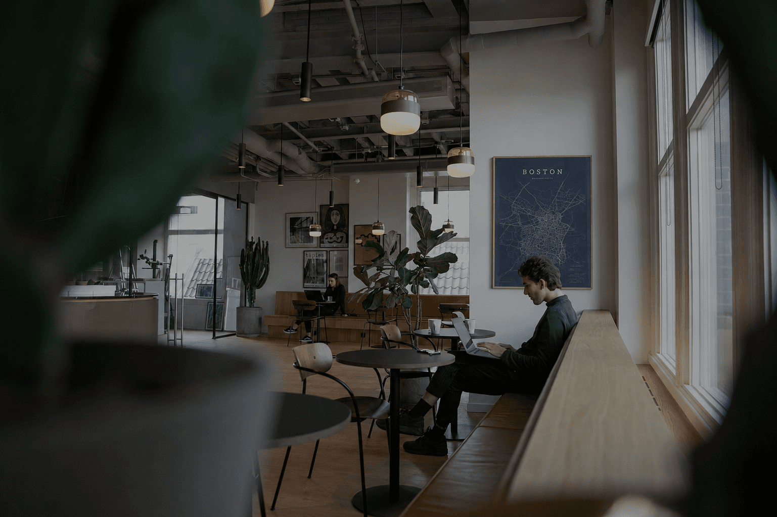 Modern workspace interior with a professional working on a laptop beneath a framed Boston city map poster, representing strategy, focus, creativity, and AI-era business growth in a clean contemporary office environment.