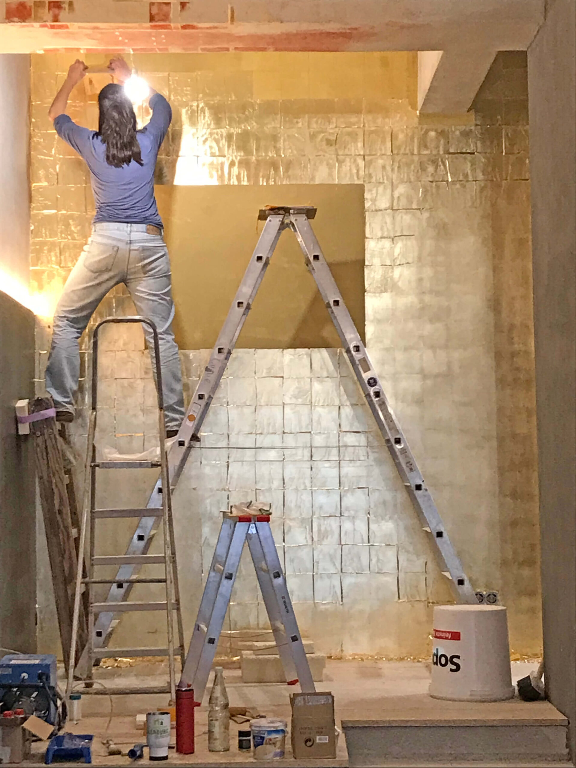 Vergoldete Wandfläche im Café Thorn während der Ausführung mit Handwerker auf einer Leiter.