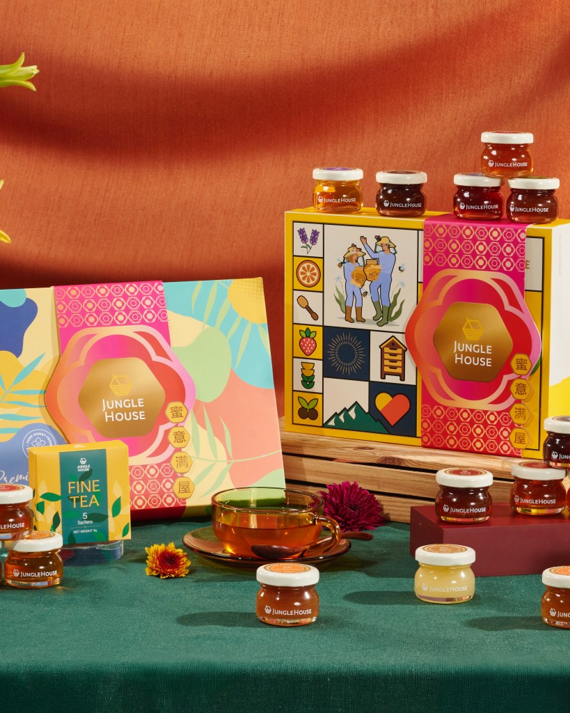 Display of colorful packaging for honey and fine tea from Jungle House, featuring jars of honey, a cup of tea, and floral decorations on a green tablecloth.