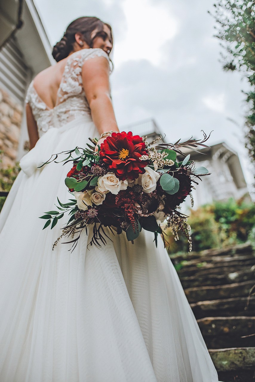 Bride in a lace wedding dress holding a vibrant bouquet of flowers on stone steps.