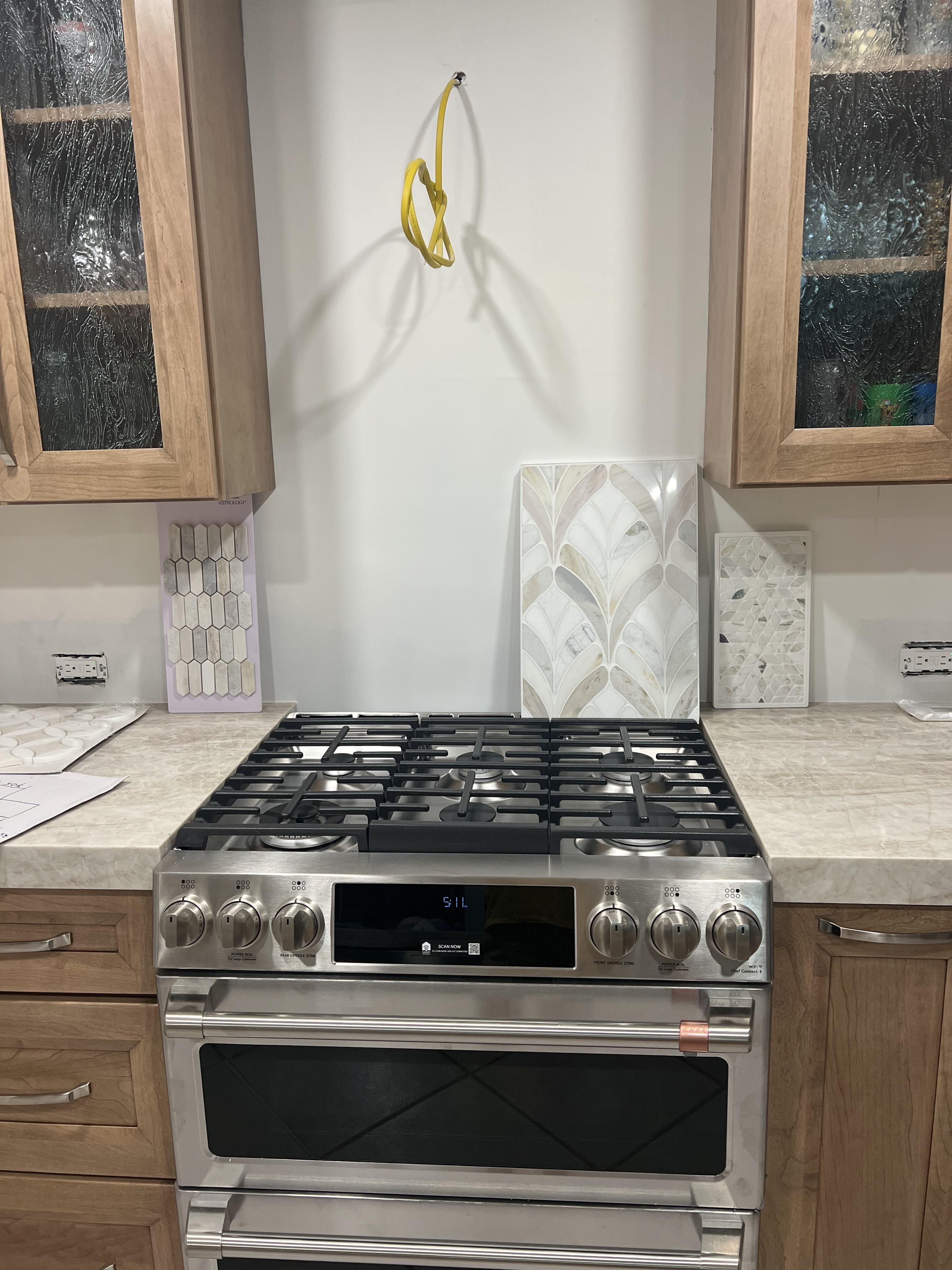 The original kitchen — warm honey cabinets, cream counters, bare backsplash wall with tile samples propped up