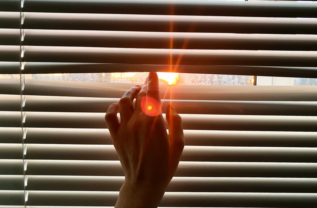 Hand separating window blind an inch to see the sunlight